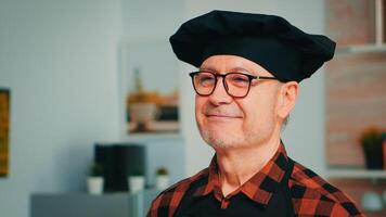 personnes âgées âge homme portant chef bonte souriant dans Accueil cuisine. proche en haut portrait de content retraité vieux boulanger avec des lunettes et tablier à la recherche à caméra prêt à cuisinier fait maison Pâtisserie avec farine et des œufs. photo