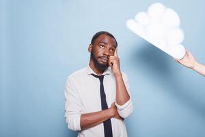 réfléchi Masculin entrepreneur à la recherche à blanc papier idée nuage concept permanent avec bras franchi et les doigts émouvant le sien diriger. Jeune noir homme réflexion suivant à pensée bulle. photo