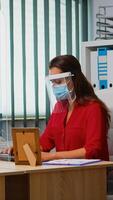 des employés portant masque et visière séance dans Nouveau Ordinaire Bureau pièce respectant social distanciation. collègues de travail travail dans moderne lieu de travail respectant protection règles contre convoitise virus en utilisant plexiglas. photo