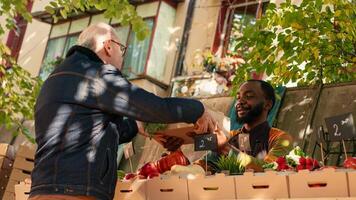 Jeune Masculin agriculteur vente boîte de biologique jardin produire à local nourriture marché, donnant coloré Frais bio des produits. personnes âgées homme achat localement grandi des fruits et des légumes. ordinateur de poche tir. photo