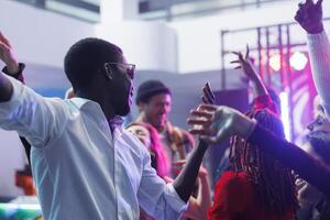 africain américain homme prise selfie ensemble avec copains tandis que faire la fête et ayant amusement dans boîte de nuit. diverse gens fabrication de bonne humeur photo tandis que aller en boîte sur bondé piste de dance