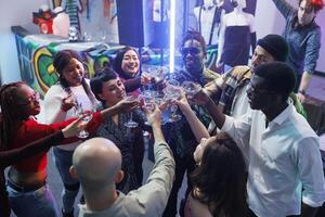 de bonne humeur copains tintement des lunettes et en disant à votre santé tandis que célébrer ensemble dans boîte de nuit. content gens en buvant de l'alcool breuvages et faire la fête sur piste de dance à club rassemblement photo