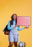 content touristique avec discours bulle icône création publicité, en voyageant sur vacances voyage avec Sacs. Jeune femelle modèle montrant fond vide papier carton avec publicité dans studio, isolé planche. photo