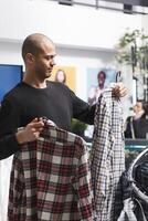 achats centre commercial boutique arabe homme client navigation plaid chemises et en portant deux tenues sur cintres. Vêtements boutique client choisir décontractée vêtements pour hommes vêtements, considérant style et en forme photo