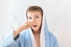 petit enfant, garçon dans une bleu éponge peignoir avec une brosse à dents sur blanche. une enfant brosses le sien dents. soins de santé et dentaire se soucier photo