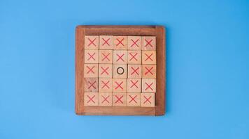 en bois Jeu planche tic-tac-toe. tournant de le des lettres xo et milieu un différent de chaque autre sur bleu Contexte. photo