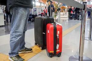 Osaka ville, Japon, 2023 -fermer jambes de touristique homme avec noir et rouge bagage attendre pour vérifier dans à Compagnie aérienne compteur à kansai international aéroport. photo