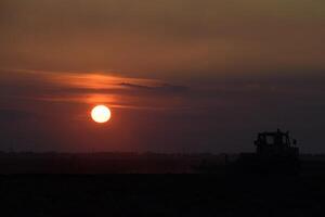 tracteur labour charrue le champ sur une Contexte le coucher du soleil. tracteur silhouette sur le coucher du soleil Contexte photo