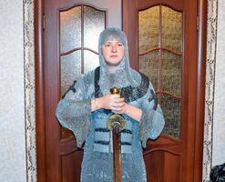 une homme habillé en haut dans une chevalier haubert à Accueil dans le sien chambre. chevalier épée dans le mains de une homme. photo