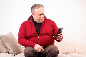 homme parlant ou en train de regarder quelque chose sur le sien téléphone tandis que séance sur le canapé photo