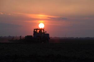 tracteur labour charrue le champ sur une Contexte le coucher du soleil. tracteur silhouette sur le coucher du soleil Contexte photo