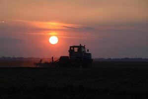 tracteur labour charrue le champ sur une Contexte le coucher du soleil. tracteur silhouette sur le coucher du soleil Contexte photo