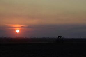 tracteur labour charrue le champ sur une Contexte le coucher du soleil. tracteur silhouette sur le coucher du soleil Contexte photo