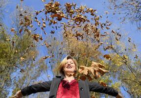 une femme jette en haut le l'automne Jaune feuilles. l'automne dans le parc photo