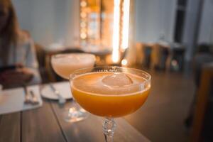 glacé Orange cocktail dans élégant verre avec confortable à manger ambiance photo