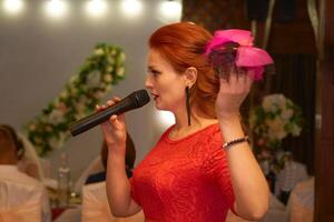 hôte de une mariage cérémonie. Jeune femme dans rouge robe avec une microphone photo