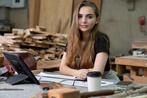 une Jeune femme est formation à être une Charpentier dans le atelier. elle travaux avec une portable ordinateur dans une bois atelier. femelle Charpentier contact les clients par téléphone intelligent. pme ordres, Commencez et petit photo