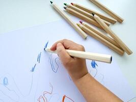 petit enfant dessine avec coloré des crayons sur papier sur blanc tableau. photo