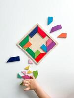 enfant main recueille multicolore en bois mosaïque sur blanc Contexte. enfant résout coloré tangram photo
