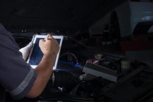 le mécanicien chèques le moteur en utilisant tablette ordinateur technologie. Achevée avec clé outil auto mécanicien travail dans le garage. réparation service. photo