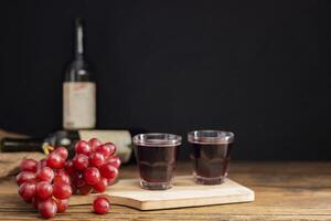 une bouquet de rouge les raisins avec rouge grain de raisin jus dans une verre mis sur une en bois table ou rouge vin, délicieux Naturel en bonne santé jus boire. photo
