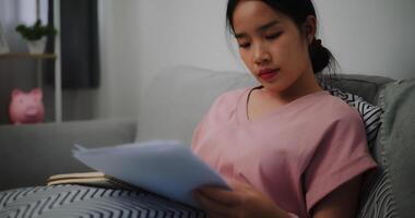 portrait de Jeune femme séance sur canapé à la recherche par Document de travail et vérification Les données et prend Remarques à Accueil Bureau photo