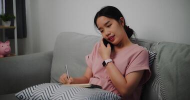 portrait de Jeune femme parlant mobile téléphone et prendre Remarques dans une carnet tandis que séance sur canapé à Accueil bureau. photo