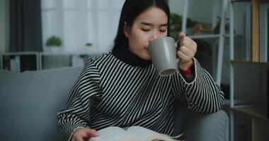 portrait de content Jeune asiatique femme en buvant Matin café ou thé et en train de lire dans vivant pièce à Accueil sur fin de semaine. loisir et style de vie, gratuit temps photo