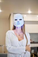 magnifique femme avoir une LED lumière thérapie masque traitement pour sa visage à maison. photo