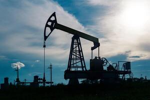 silhouette de une Pumpjack sur un pétrole bien contre le Contexte de ciel photo