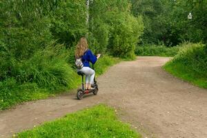 Jeune femme monte un électrique scooter le long de le chemin dans le parc photo