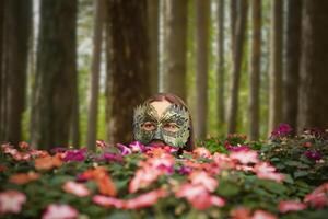 Jeune femme dans une mystérieux masque parmi fleurs sur une floue forêt Contexte photo