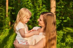 Jeune femme affectueusement regards à sa peu fille, lequel elle détient dans sa bras, contre le Contexte de la nature photo