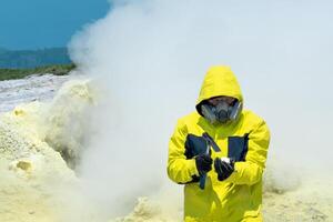 homme volcanologue sur le Contexte de une fumeur fumerolle examine une échantillon de une soufre minéral avec une géologique marteau photo