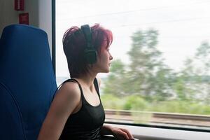 Jeune femme monte sur une banlieusard train et regards en dehors le fenêtre à un à l'extérieur paysage flou dans mouvement photo