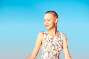 fille adolescent dans une robe avec une court la Coupe de cheveux à la recherche dans le distance, plisser les yeux à le soleil, contre le Contexte de le ciel photo