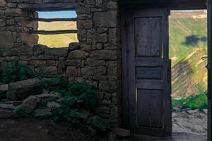 en bois porte dans le ruines de un abandonné maison par lequel montagnes sont visible, dans le ruines de le fantôme village de gamsutl dans Daghestan photo