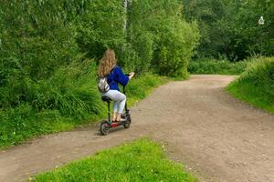 Jeune femme monte un électrique scooter le long de le chemin dans le parc photo