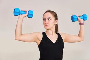 Jeune femme effectue un exercice avec haltères contrôler sa mouvements, demi-longueur portrait sur une lumière Contexte photo