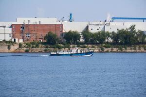 industriel paysage avec une usine sur le banques de le rivière, le long de lequel une bateau à moteur flotteurs photo