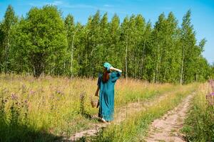 Jeune femme dans populaire paysan vêtements avec une osier panier des promenades le long de une champ route photo