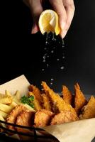 poisson et frites sur noir Contexte avec éclaboussure citron sur main photo