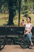 content Jeune asiatique femme tandis que équitation une vélo dans une ville parc. elle sourit en utilisant le vélo de transport. écologiquement amical concept. photo