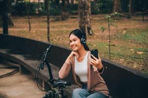 content Jeune asiatique femme tandis que équitation une vélo dans une ville parc. elle sourit en utilisant le vélo de transport. écologiquement amical concept. photo