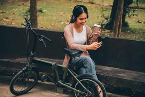 content Jeune asiatique femme tandis que équitation une vélo dans une ville parc. elle sourit en utilisant le vélo de transport. écologiquement amical concept. photo