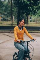 content Jeune asiatique femme tandis que équitation une vélo dans une ville parc. elle sourit en utilisant le vélo de transport. écologiquement amical concept. photo