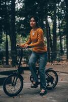 content Jeune asiatique femme tandis que équitation une vélo dans une ville parc. elle sourit en utilisant le vélo de transport. écologiquement amical concept. photo