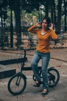 content Jeune asiatique femme tandis que équitation une vélo dans une ville parc. elle sourit en utilisant le vélo de transport. écologiquement amical concept. photo