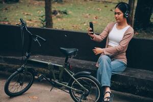 content Jeune asiatique femme tandis que équitation une vélo dans une ville parc. elle sourit en utilisant le vélo de transport. écologiquement amical concept. photo