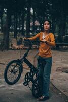 content Jeune asiatique femme tandis que équitation une vélo dans une ville parc. elle sourit en utilisant le vélo de transport. écologiquement amical concept. photo